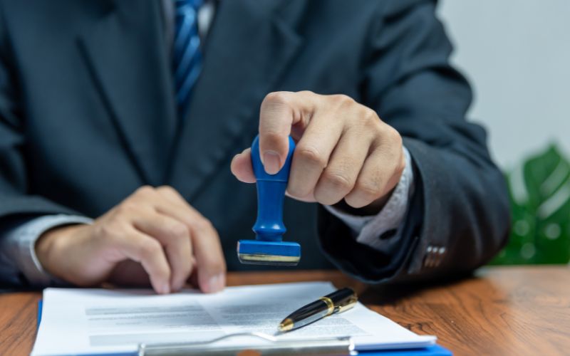 Man stamping approved visa application document with blue rubber stamp on a desk