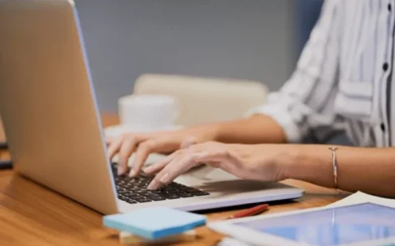 Woman working on laptop with tablet and stationery on desk