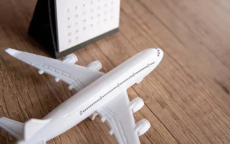 Toy airplane next to a calendar on a wooden table, symbolizing travel planning